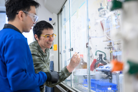 Alison Wendlandt writes on a window in a lab, next to a student.