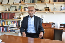 Emery Brown sits at a desk with shelves full of books and mementos behind him