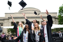 Graduating students in gowns toss their caps in the air.