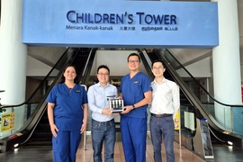 Four people pose in front of two escalators and a sign that says "Children's Tower." The two in the center hold a toaster-sized device.
