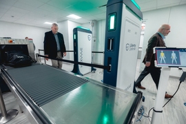 Two individuals walk past a security screening system.