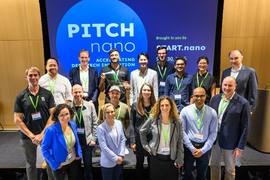 17 people pose on a small stage with "Pitch nano" on a screen behind them