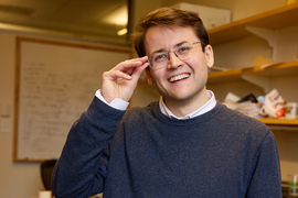 Photo of Alexander Busch in an office with his right hand on the frame of his glasses 