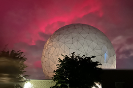 Pink sky at night with clouds, seen behind a large radome attached to Haystack Observatory