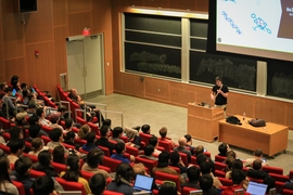 Hannes Stärk stands in front of a slide presentation in front of a large audience inside of a packed lecture hall.