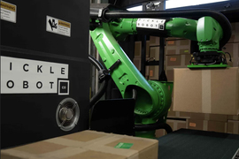 Green robot arm lifts cardboard box via suction.