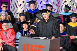 Alejandro Aravena stands at an indoor MIT lectern. MIT faculty members sit behind him. All wear academic regalia.
