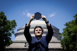 Pablo Jarillo-Herrero stands in front of the MIT dome, holding a circular wafer displaying moire patterns over his head
