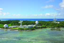 Two radar domes and two radar dishes sit on a tropical island on a sunny day