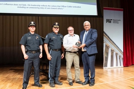 Anantha Chandrakasan presents an award to Michael Grenier, flanked by two MIT police officers in uniform on stage