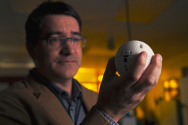 In a darkened lab, Jude Kelley holds up a white baseball-sized spherical sensor