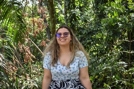 Hana Sousa sits in front of green trees in a rainforest on a sunny day 