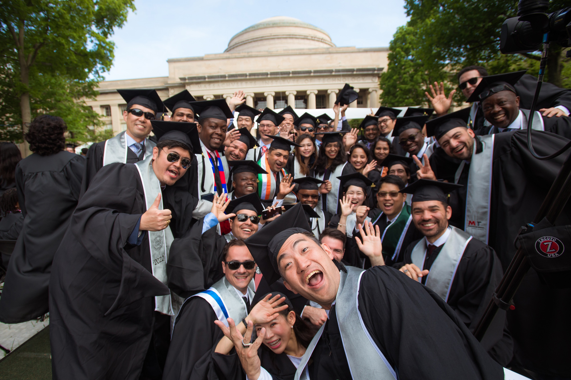 Crowd of graduates in caps and gowns smiling and waving.