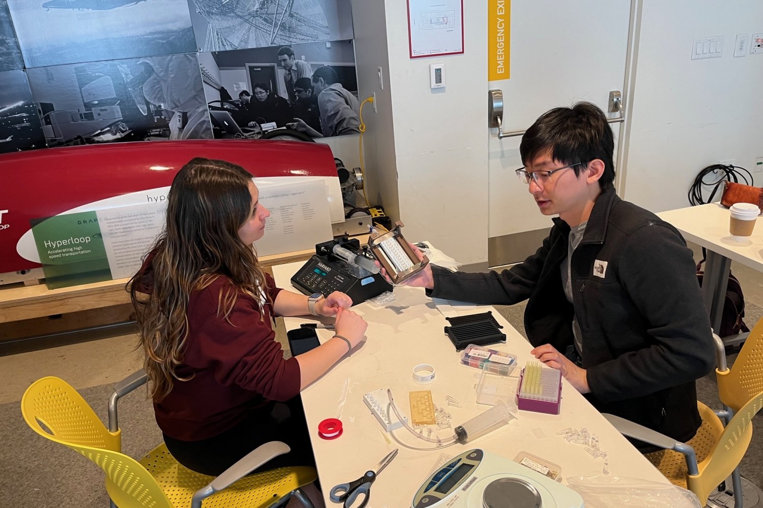 MIT students Rachael Rosco (left) and Brandon Sun work on a droplet-dispensing manifold inside the MIT Lincoln Laboratory Beaver Works Center on MIT campus.