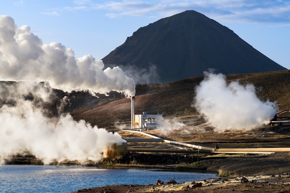 Workers stand near geothermal drilling equipment at an energy site.