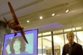 Senior research engineer Charles M. Oman reflects on the loss of his friend, astronaut Laurel Clark, at MIT's memorial observance Monday. Clark's image was shown on a screen behind a model of a monoplane hanging in the Gelb Learning Center.