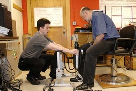 Dustin Williams (MIT S.M. 2001), of Interactive Motion Technologies Inc., helps Hermano Igo Krebs, a principal research scientist in MIT's mechanical engineering department, put on the Anklebot, a robotic device designed to help stroke patients regain movement in paralyzed ankles.