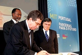 Jose Mariano Gago, the Portuguese minister of science, technology and higher education, at left, signs a document signalling a collaboration between MIT and many of Portugal's top national universities. At rear, MIT Chancellor Phillip Clay and JoÃ£o Sentieiro, chairman of the board of the MIT-Portugal Program, look on.