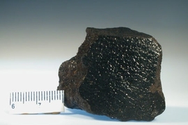 A picture of the first discovered (and therefore eponymous) angrite "Angra dos Reis"; which was observed to fall from the sky in 1869 near the town of Angra dos Reis in Brazil.Â  The black; shiny face was produced from melting of the meteorite's surface during passage through Earth's atmosphere.Â  Scale bar is in centimeters.