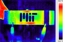 Infrared themographic image of a nanoengineered composite heated via electrical probes (clips can be seen at bottom of image). The scalebar of colors is degrees Celsius. The MIT logo has been machined into the composite, and the hot and cool spots around the logo are caused by the thermal-electrical interactions of the resistive heating and the logo "damage" to the composite. The enhanced thermogr...