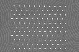A scanning electron microscope image shows a pattern produced by the MIT team's self-assembling polymer system. A grid of posts, seen as light-colored circles, controls the size and spacing of structures on the surface. Cylinders outside the grid form quite different shapes than those inside it, which are controlled by the posts.