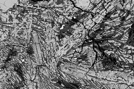An electron micrograph image of a meteorite sample from the asteroid Vesta. Dark, finely striated regions represent rapidly cooled material. Light-colored crystals represent a second slower-cooling period, in which an ancient dynamo may have resided.