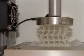 A 3D-printed soft, flexible scaffold that is coated in wax and is being compressed in a temperature-controlled chamber. Heating a composite whose wax coating has broken can enable the wax to soften and "heal" to restore its original strength and properties.

