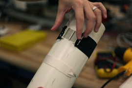 Several actuators aligned into a 3-D-printed cartridge structure, paired with passive fabric to form an active tourniquet, and mounted on a rigid object approximating a human limb.