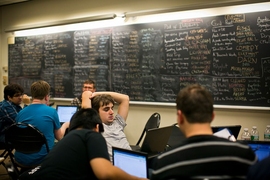 PuzzFeed member James Wiken '13 (center) and his teammates work away; behind them, solved puzzles are listed on the blackboard. 