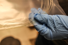 Graduate student Chong Hou holds a bag of drawn fibers. The fibers are as thin as 100 micrometers in diameter, and the material coating further enhances the strength of the fibers.