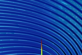 By using plasmons to “wiggle” a free electron in a sheet of graphene, researchers have developed a new method for generating X-rays. In this image of one of their simulations, the color and height represent the intensity of radiation (with blue the lowest intensity and red the highest), at a moment in time just after an electron (grey sphere) moving close to the surface generates a pulse.