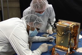 MIT graduate students Pronoy Biswas (left) and Mark Chodas prepare the REgolith X-Ray Imaging Spectrometer (REXIS) instrument for flight. 