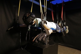 A user experiences the underwater world using Amphibian SCUBA diving simulator. The user is resting on a suspension system wearing Oculus Rift, a snorkel with breathing sensor, and gloves for motion detection. 