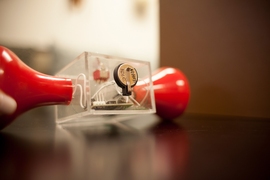 To demonstrate the supercapacitor's ability to store power, the researchers modified an off-the-shelf hand-crank flashlight (the red parts at each side) by cutting it in half and installing a small supercapacitor in the center, in a conventional button battery case, seen at top. When the crank is turned to provide power to the flashlight, the light continues to glow long after the cranking stops, ...