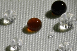 Repellency of different liquids on polyester fabric coated with H1F7Ma-co-DVB: soy sauce (black drop), coffee (brown drop), HCl acid (top left transparent drop), NaOH (bottom right transparent drop) and water (remaining transparent drops).