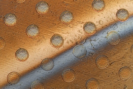 This photo shows circles on a graphene sheet where the sheet is draped over an array of round posts, creating stresses that will cause these discs to separate from the sheet. The gray bar across the sheet is liquid being used to lift the discs from the surface.