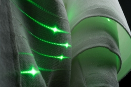 In this photograph of fabric, you can see the green light of functional fibers. “No human-made objects are more ubiquitous or exposed to more vital data than the clothes we all wear,” says doctoral student Gabriel Locke. “Wouldn’t it be great if we could somehow teach our fabrics to sense, store, analyze, extract and communicate this potentially useful information?”