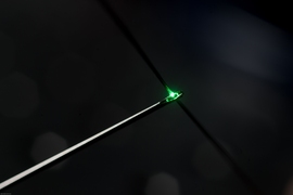 A thread of functional fiber glows green and passes through the head of a sewing needle.