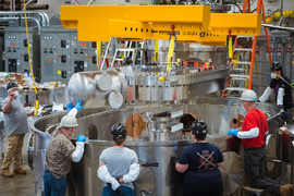 Five workers standing around the basin-like test stand that will hold the magnet