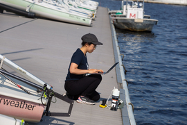 Charlene Xia kneeling on a dock, facing the water and typing on a laptop. 