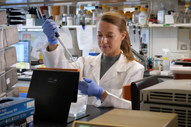 Woman in a white lab coat, working in a lab and holding a pipette 