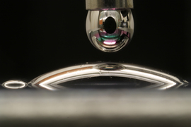 One droplet of liquid mercury hangs from a dropper; below, another droplet spreads out on a surface.