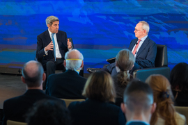 John Kerry and Rafael Reif sitting in armchairs on a stage, facing each other
