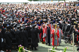 Graduation procession makes its way through a crowd, the leader is holding MIT’s golden ceremonial mace