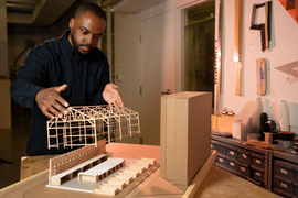 Photo of Justin Brazier holding a wooden stick model of a building just over the base of the model