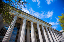 From-the-ground view of MIT entrance, with Greek-style columns reaching upward against a blue sky