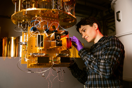 Alex Greene wears purple latex gloves while tinkering with a complex golden contraption with wires sticking out.