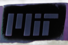 A closeup of a sheet of black carbon with lumpy edges, and the MIT logo appears as if embossed in grey.