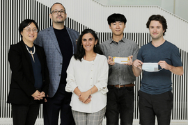 Group photo of five researchers, and two are holding surgical masks that incorporate their devices. Background is a black-and-white striped wall.