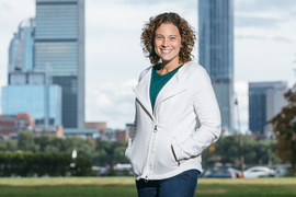 Danna Freedman smiles while standing outside, with trees, cloudy sky, and Boston skyline in background. 